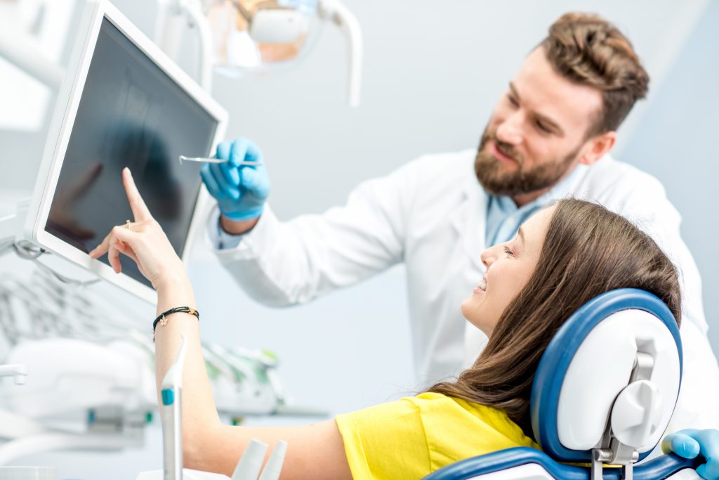 Dentist showing young woman patient tooth x-ray on the monitor at the dental office